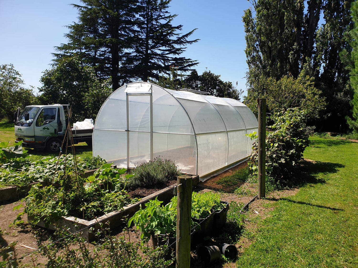 Greenhouse in a garden with trees and a truck in the background